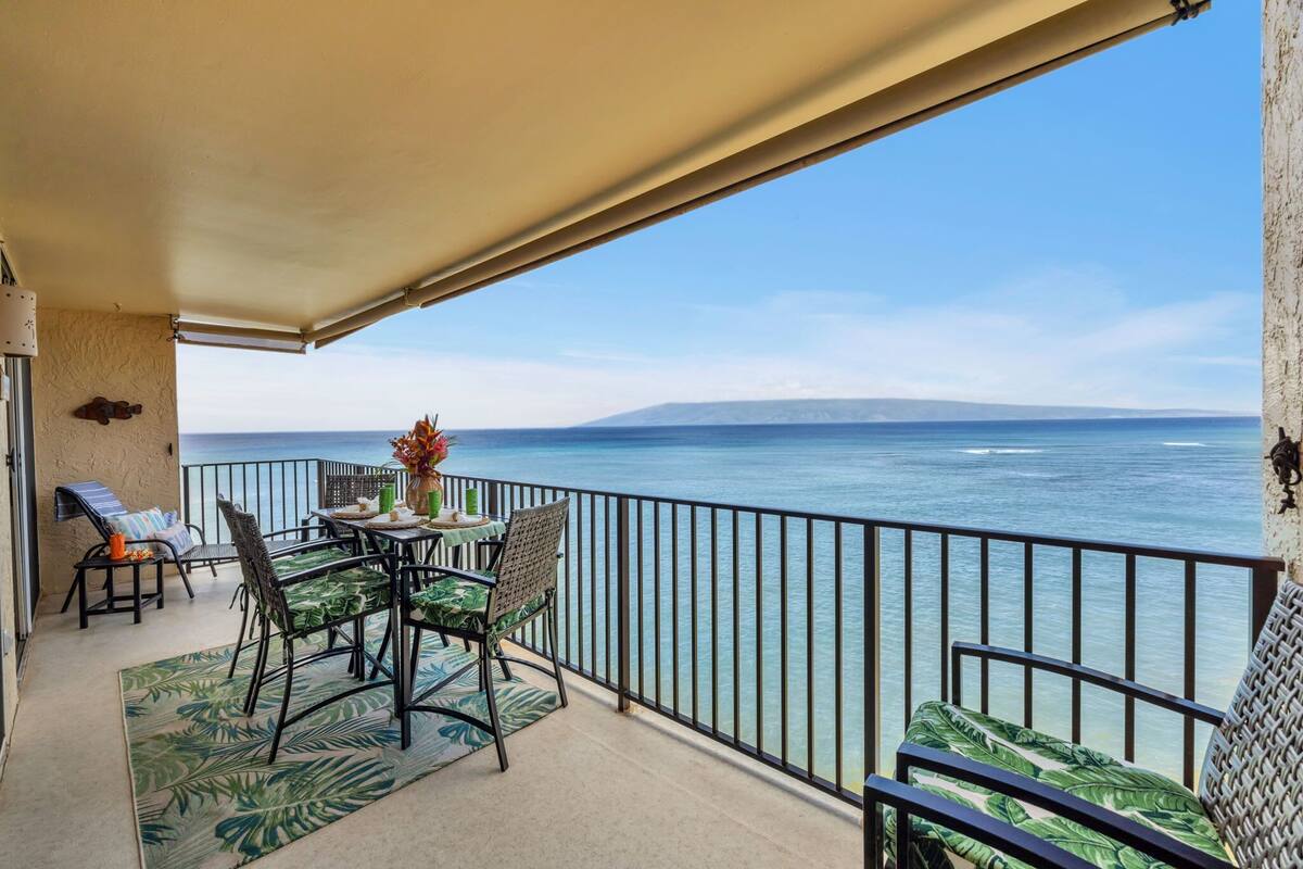 A balcony with a view of the sea, a table with chairs, and a small table with a vase of flowers.