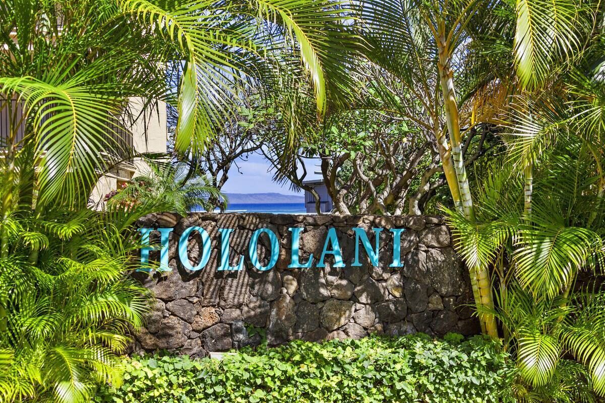 Un muro de piedra con el nombre "HILO LANI" en letras grandes, rodeado de exuberante follaje tropical.