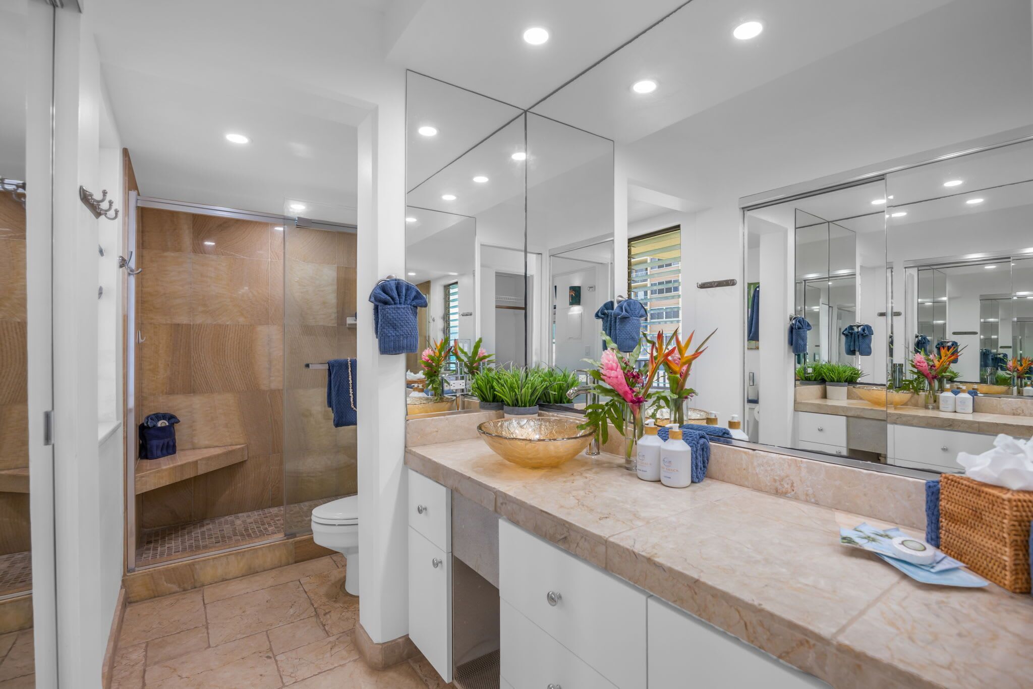 A modern bathroom with a glass shower enclosure, a large mirror, and a marble countertop.