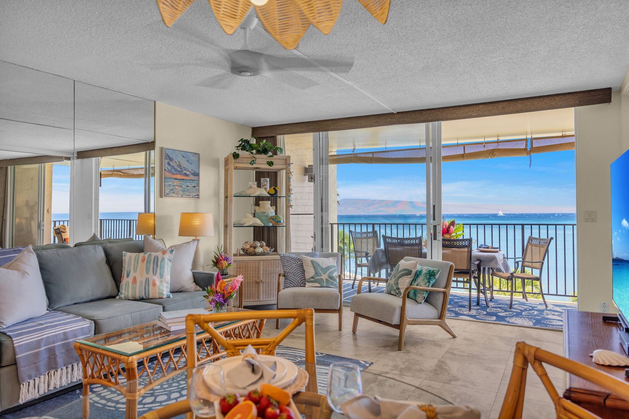 A spacious living area with a balcony overlooking the sea, furnished with a sofa, chairs, and a dining table.