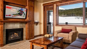 Una sala de estar acogedora con chimenea, televisor y un ventanal con vistas a un paisaje nevado.