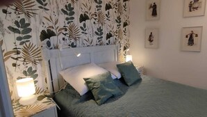 Een slaapkamer met een bed, kussens, een nachtkastje, een lamp en lijstwerken aan de muur.