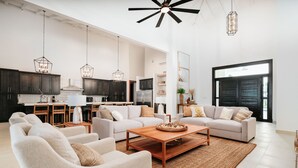 A spacious living area with a sofa set, coffee table, and a kitchen in the background.