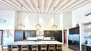 A spacious kitchen with a large island, dark cabinets, stainless steel appliances, and pendant lighting.