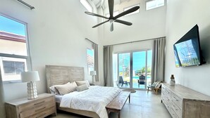 A spacious bedroom with a large bed, a ceiling fan, a TV, and a view of the outdoors.