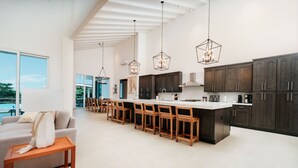 A modern kitchen with dark cabinets, a long island, and pendant lighting.