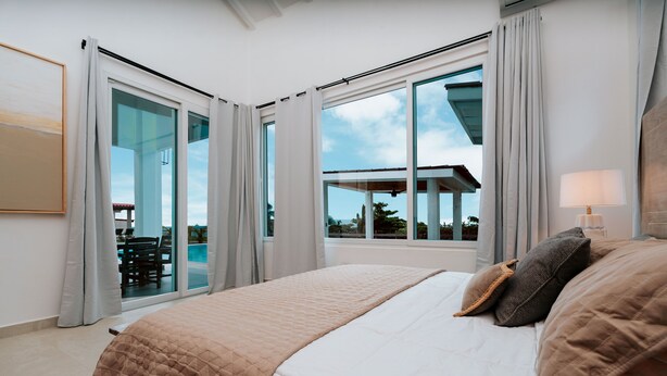 A bedroom with a large bed, a sliding glass door leading to a balcony, and a view of the outdoors.