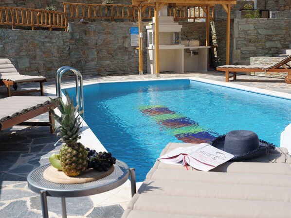Un espace piscine comprenant des chaises longues, une pergola en bois et un mur en pierre.