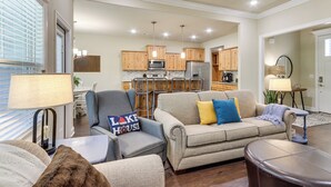 A modern living room with a sofa, armchairs, and a coffee table. There is a kitchen in the background with wooden cabinets and a refrigerator. - Modern Family Cabin: Walk to Table Rock Lake (Eureka Springs)