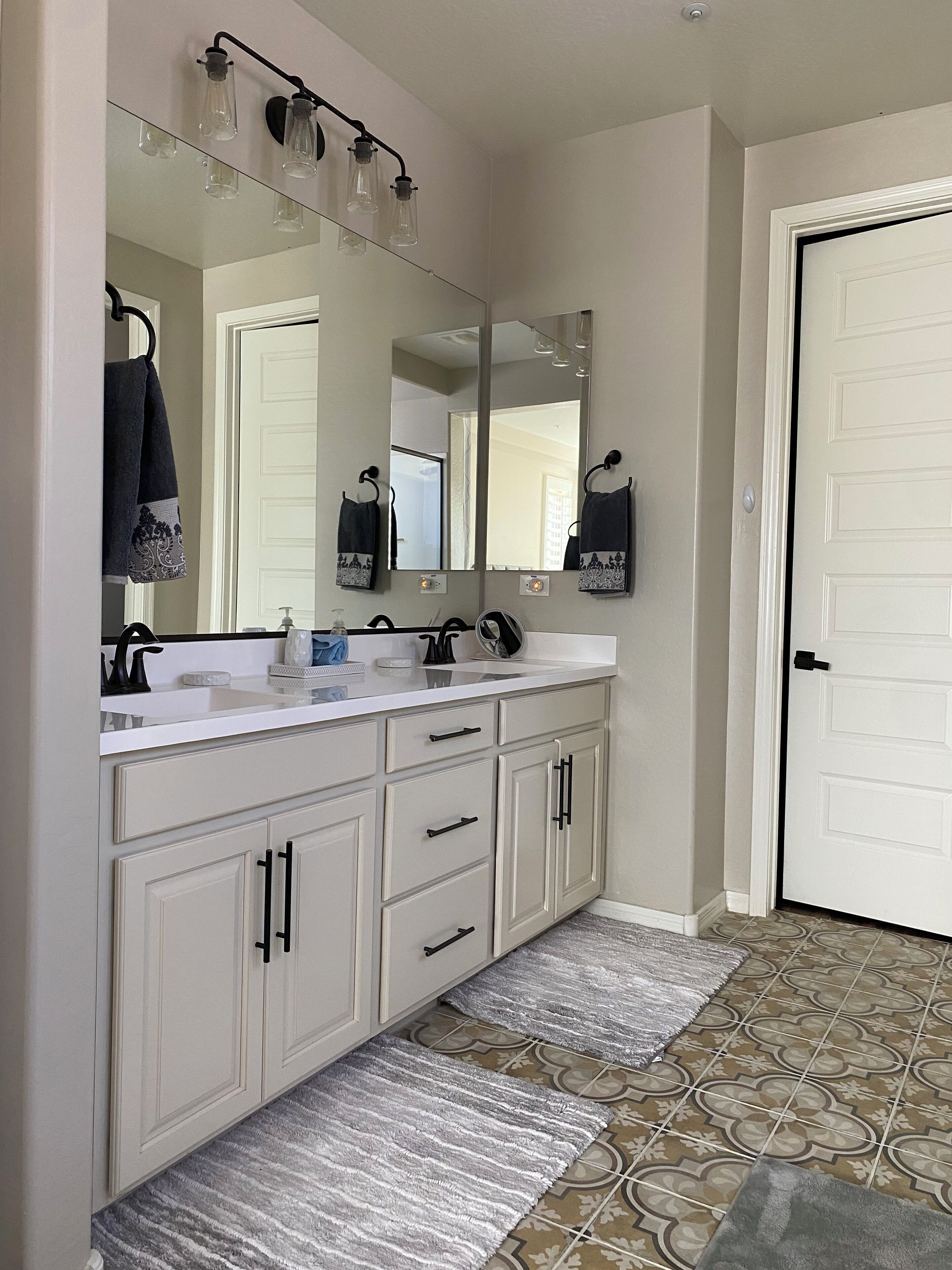 A bathroom with a white vanity, a large mirror, and a door.