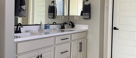 A bathroom with a white vanity, a large mirror, and a door.