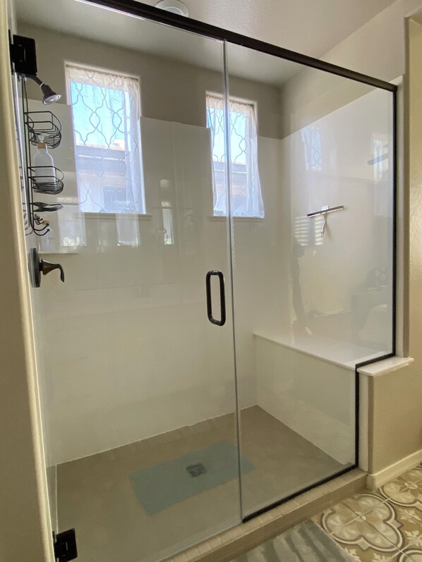 Un área de ducha con mampara de vidrio, un perchero y un ventanal con un diseño decorativo.
