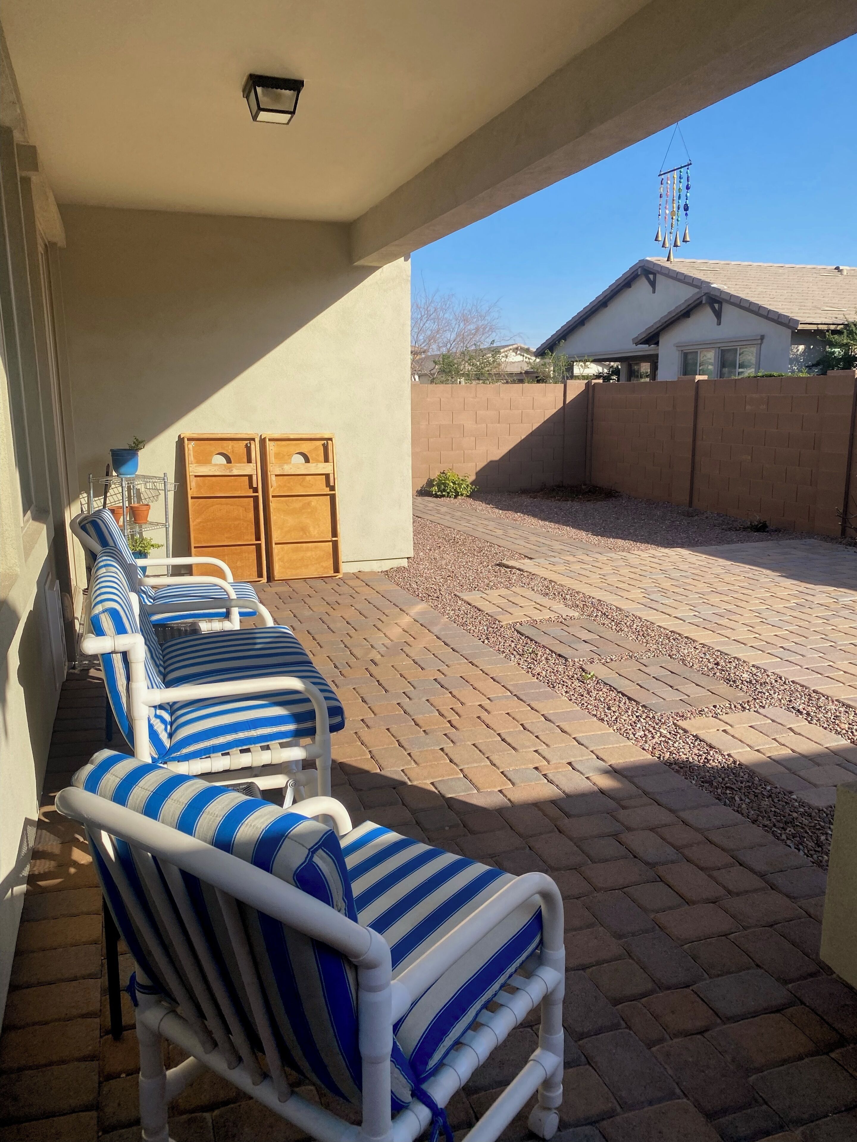 A covered patio with striped lounge chairs, a metal plant stand, and a brick wall.