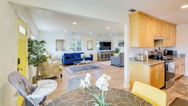 A spacious living area with a blue sofa, a dining table with orchids, and a kitchen with wooden cabinets and modern appliances. - Business/Family Retreat Near Levi's Stadium! (Santa Clara)
