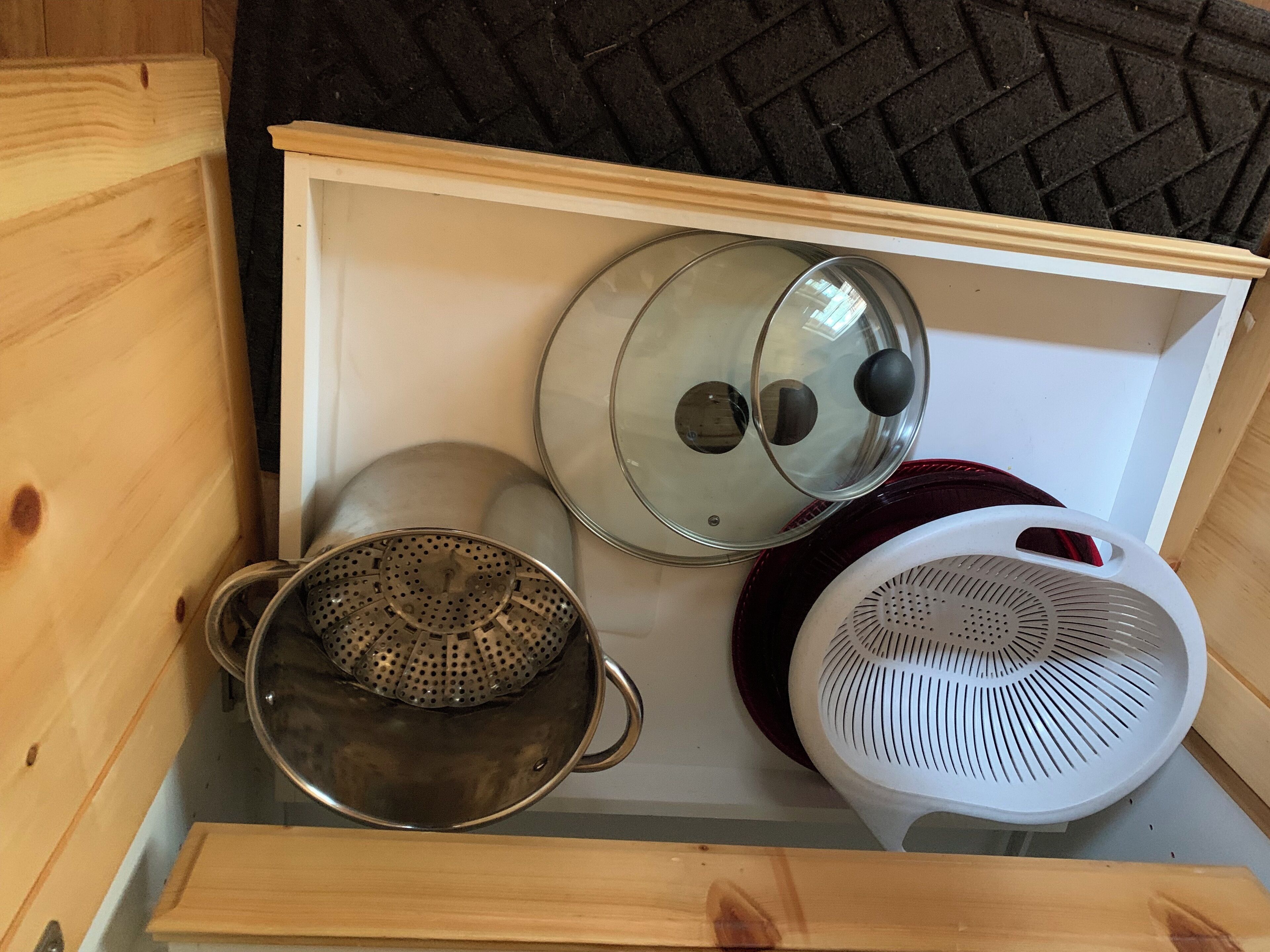 A wooden chest with kitchen utensils including a colander, a pot with a lid, and a white strainer.