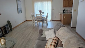 A modern living room with a grey sofa, a glass coffee table, and a dining area with a table and chairs. - Charming 3-bedroom house MUST BE A LAND OWNER IN EAGLE ROCK RESORT (Hazleton)