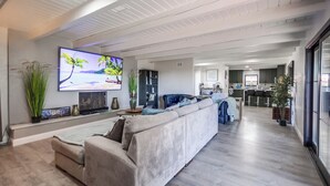 Una sala moderna con un televisor de pantalla plana grande, un sofá seccional beige y una cocina al fondo.
