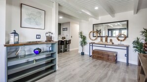 Una habitación amplia con piso de madera, un espejo grande, una consola decorada con adornos y una obra de arte enmarcada en la pared.