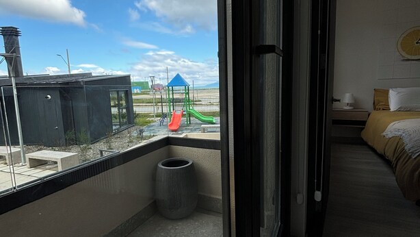A balcony with a wooden table, a trash bin, and a view of a playground with a slide and a blue-roofed structure. - Apartment By Toore Patagonia (Natales)