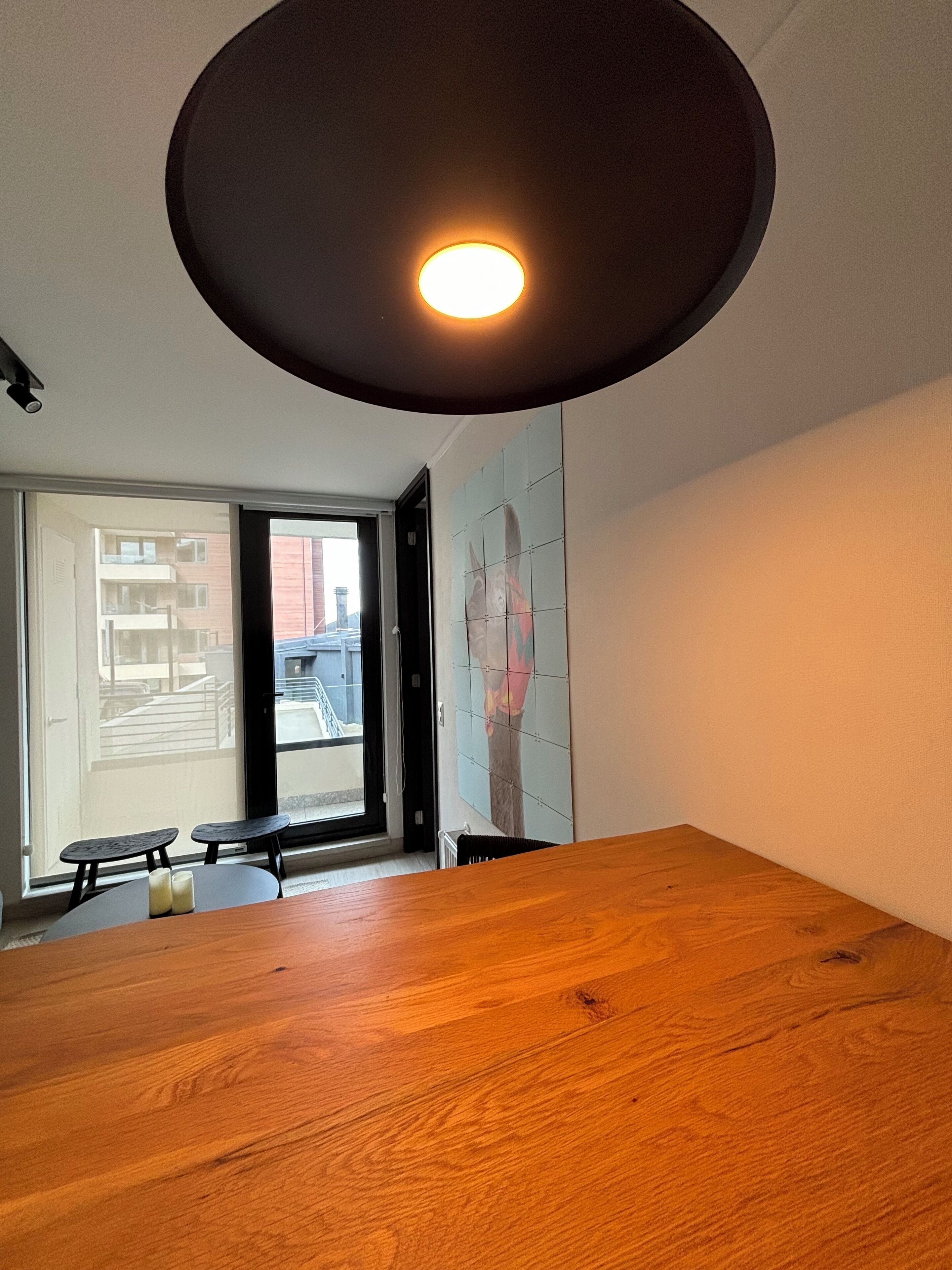 A room with a wooden table, a ceiling light, a sliding glass door, and a tiled wall.
