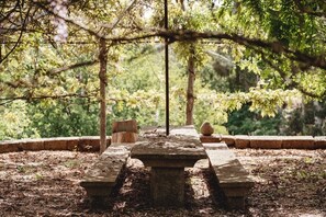 A stone picnic table in a wooded area with benches and a stone wall in the background. - Tojeira Farmhouse (Mondrões)
