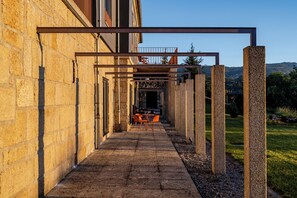 A stone building with a paved walkway leading to a covered outdoor seating area with chairs. - Tojeira Farmhouse (Mondrões)