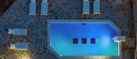 Vista aérea de una piscina con paredes de azulejos y piso de piedra, rodeada de sillones de descanso y una terraza de madera.