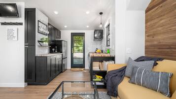 Une cuisine moderne avec des meubles de couleur sombre, un coin repas avec un canapé jaune et des coussins à motifs, et une porte visible donnant sur un espace extérieur.