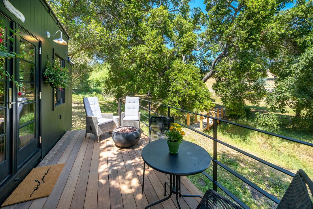 Une terrasse en bois avec des sièges d’extérieur, un pot de fleurs et une vue sur une rivière.