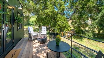 Une terrasse en bois avec des sièges d’extérieur, un pot de fleurs et une vue sur une rivière.