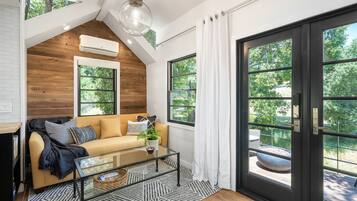Un salon moderne avec un plafond en bois, un canapé, une table basse en verre et de grandes fenêtres.