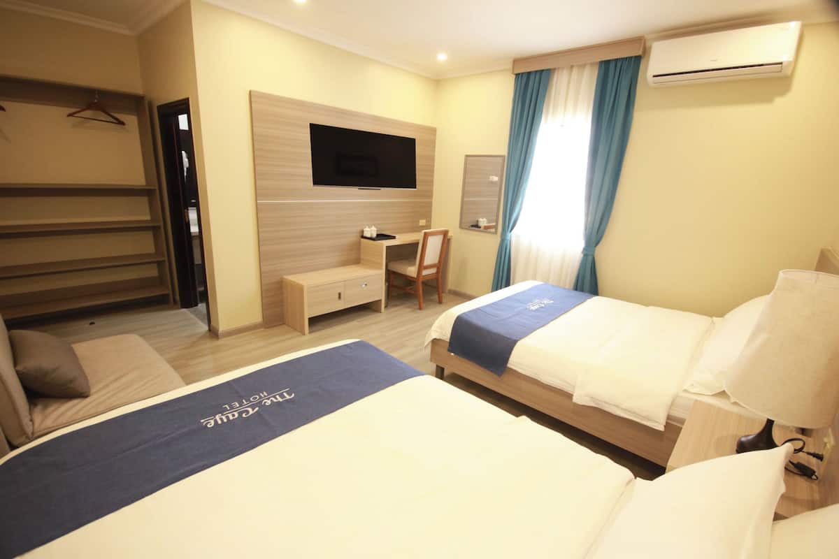 A hotel room with two beds, a desk, a chair, a TV, and an air conditioning unit.