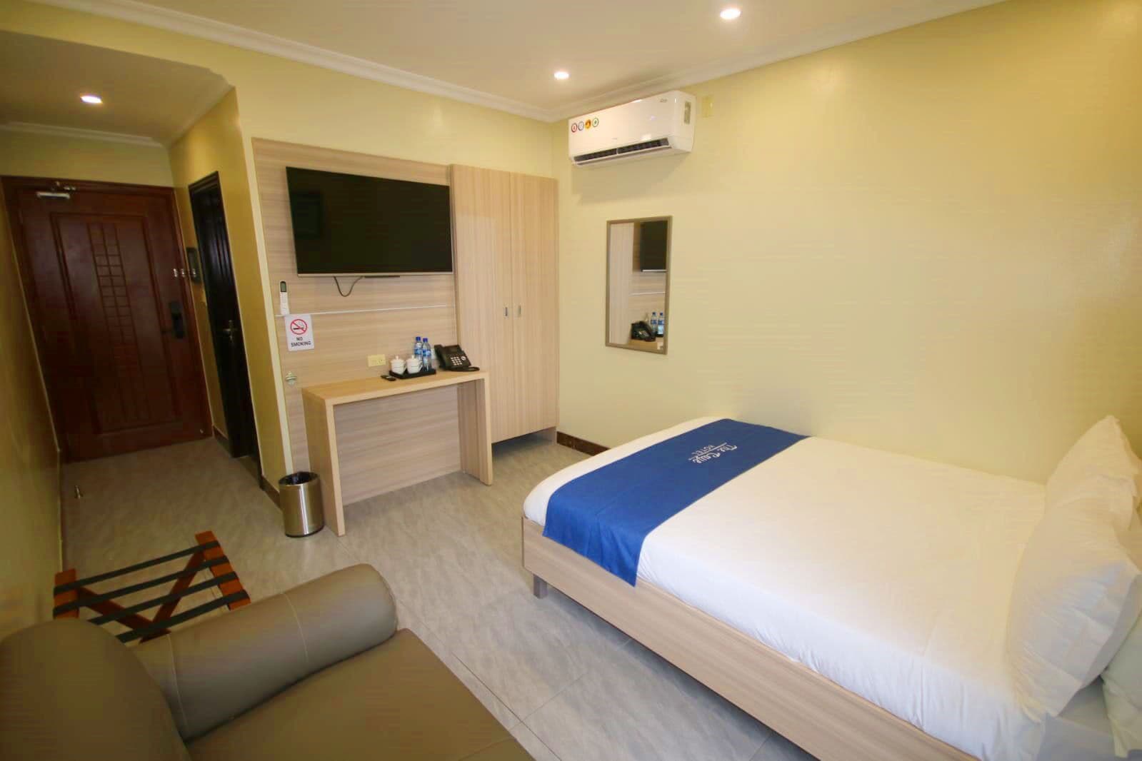 A hotel room with a bed, a desk, a television, and an air conditioning unit.