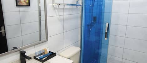 A modern bathroom with a white vanity, a large mirror, a toilet, and a glass-enclosed shower area.