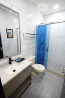 Een moderne badkamer met een witte wastafel, een grote spiegel, een toilet en een douchecabine met glazen wanden.