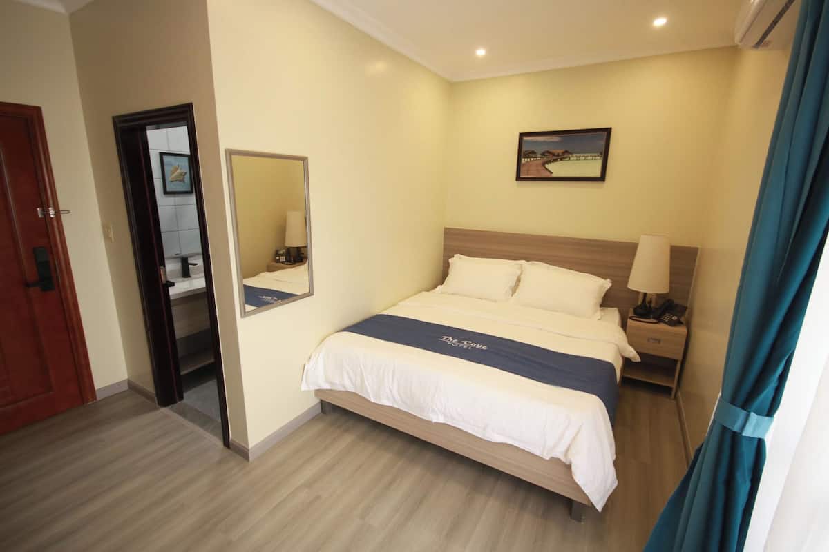 A hotel room with a bed, a nightstand with a lamp, a mirror, and a painting on the wall.