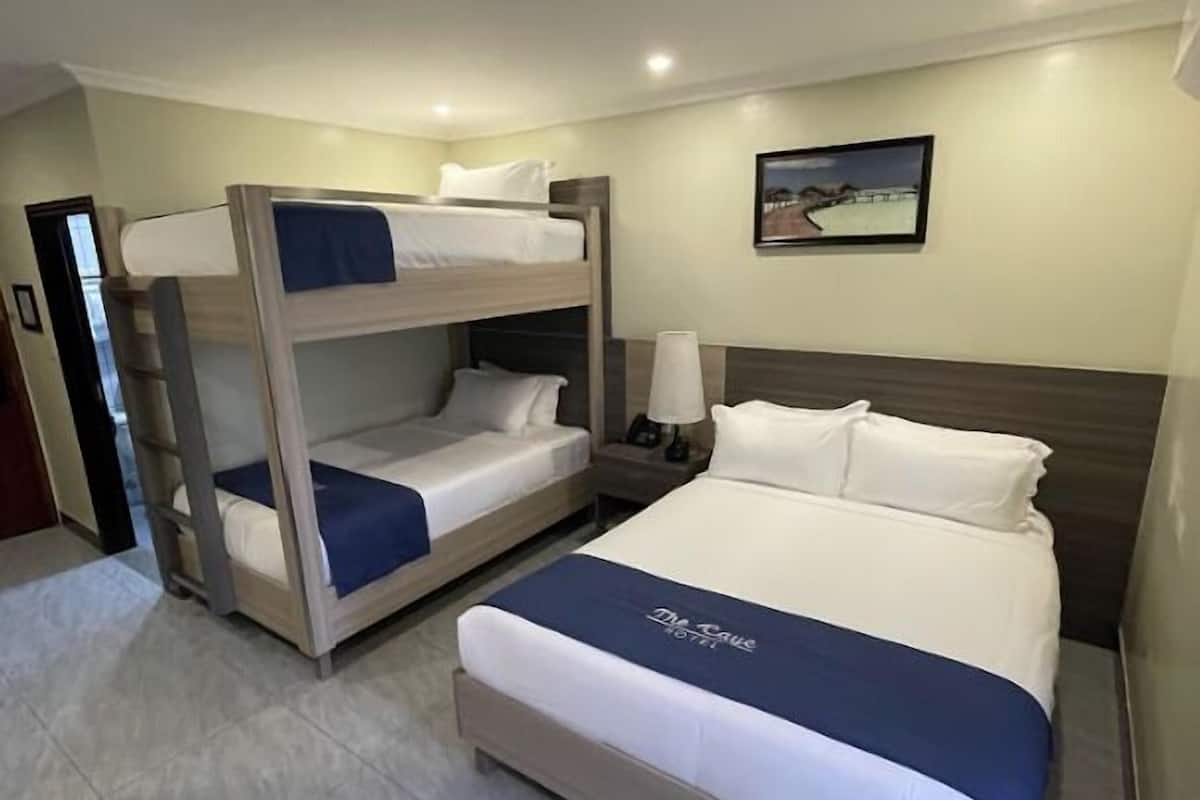 A hotel room with a bunk bed, a single bed, a nightstand with a lamp, and a framed picture on the wall.