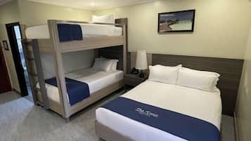 Habitación de hotel con literas, una cama individual, una mesita de noche con lámpara y un cuadro enmarcado en la pared.