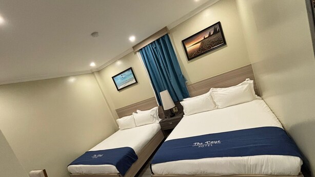 A hotel room with two beds, a nightstand, a lamp, a framed picture, and a window with curtains. - The Caye Hotel San Pedro (San Pedro)