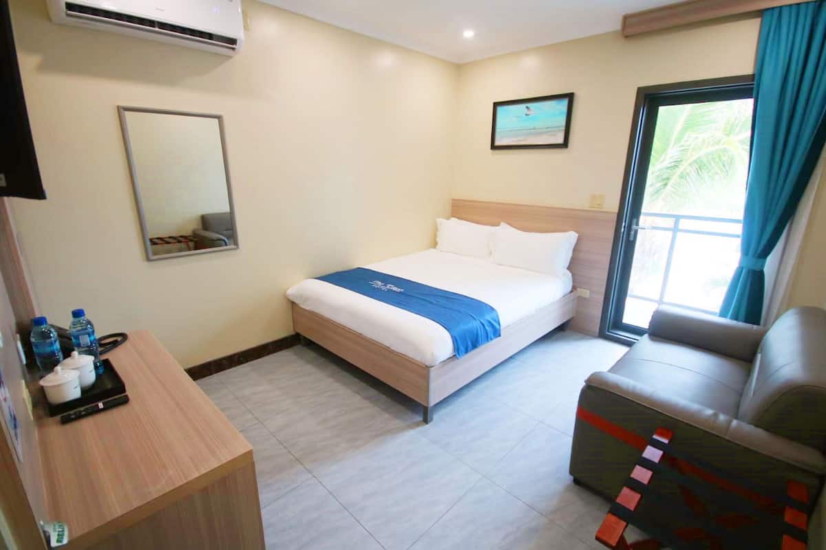 A hotel room with a bed, a desk with water bottles, a chair, and a window with curtains.