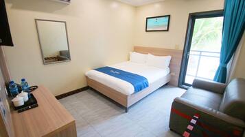 A hotel room with a bed, a desk with water bottles, a chair, and a window with curtains.