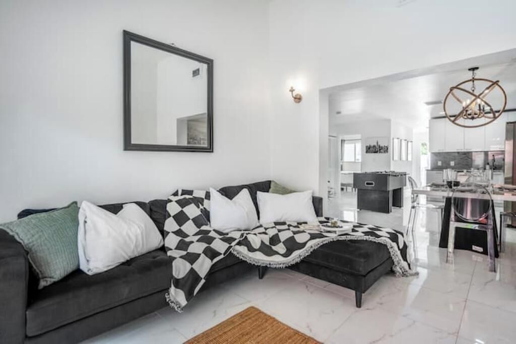 A modern living room with a black and white checkered sofa, a large mirror, and a kitchen in the background.