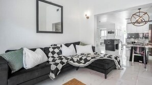 A modern living room with a black and white checkered sofa, a large mirror, and a kitchen in the background. - Stylish artistic house, close to Wynwood, Downtown (MIAMI)