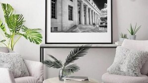 A framed black and white photograph of a building with columns, displayed above a round table with a plant and books, flanked by two armchairs with fluffy cushions. - Stylish artistic house, close to Wynwood, Downtown (MIAMI)