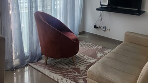 A living room with a flat-screen TV on a stand, a red chair, and a beige sofa. - Beautiful apartment to rest and vacation near puerto colombia. (Atlántico)