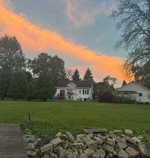 A house with a front porch, a lawn, and a stone wall in the foreground. - Cozy Riverfront Retreat (Suamico)
