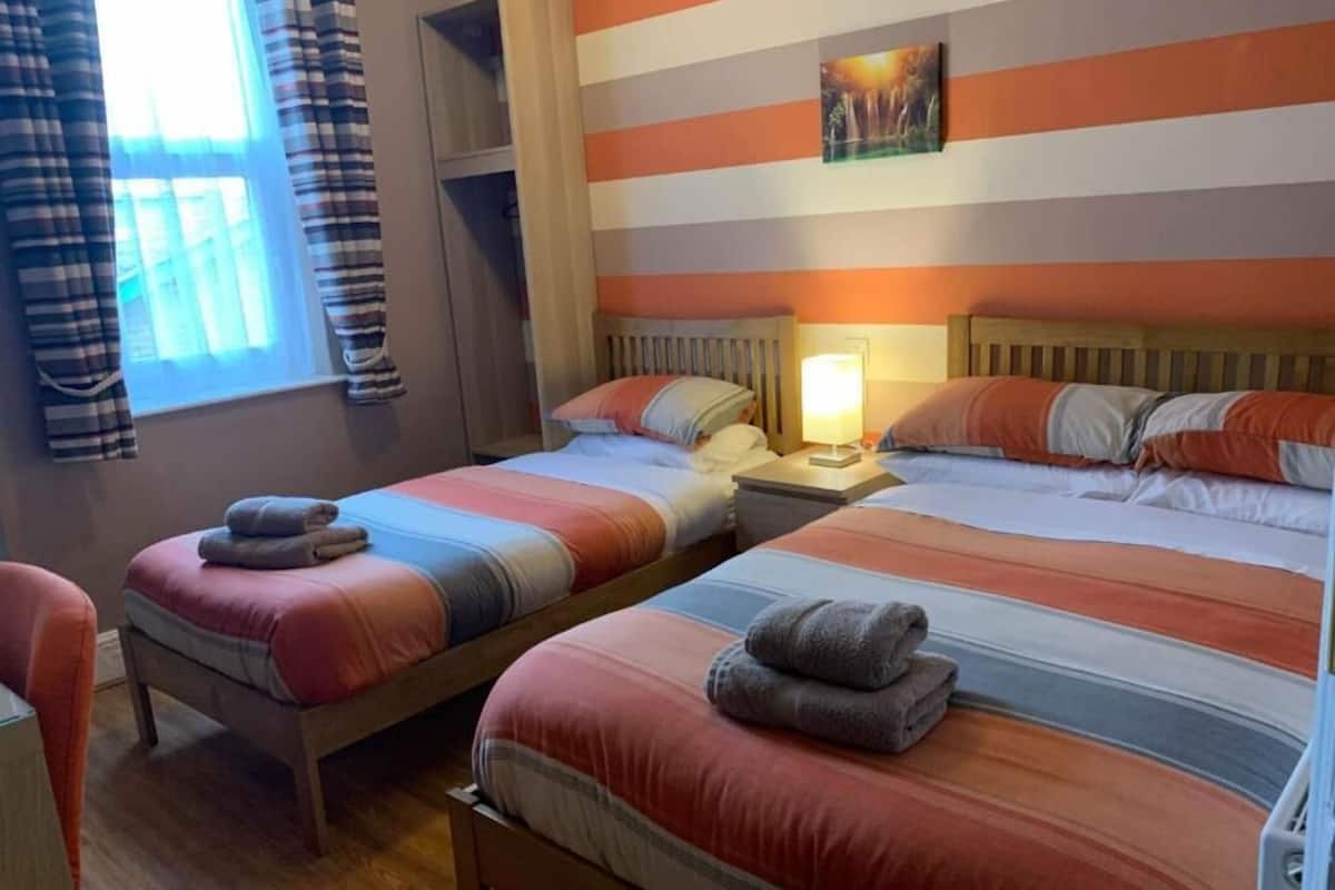 Una habitación doble con dos camas, cada una con ropa de cama y almohadas a rayas, una mesita de noche con lámpara y un cuadro en la pared.