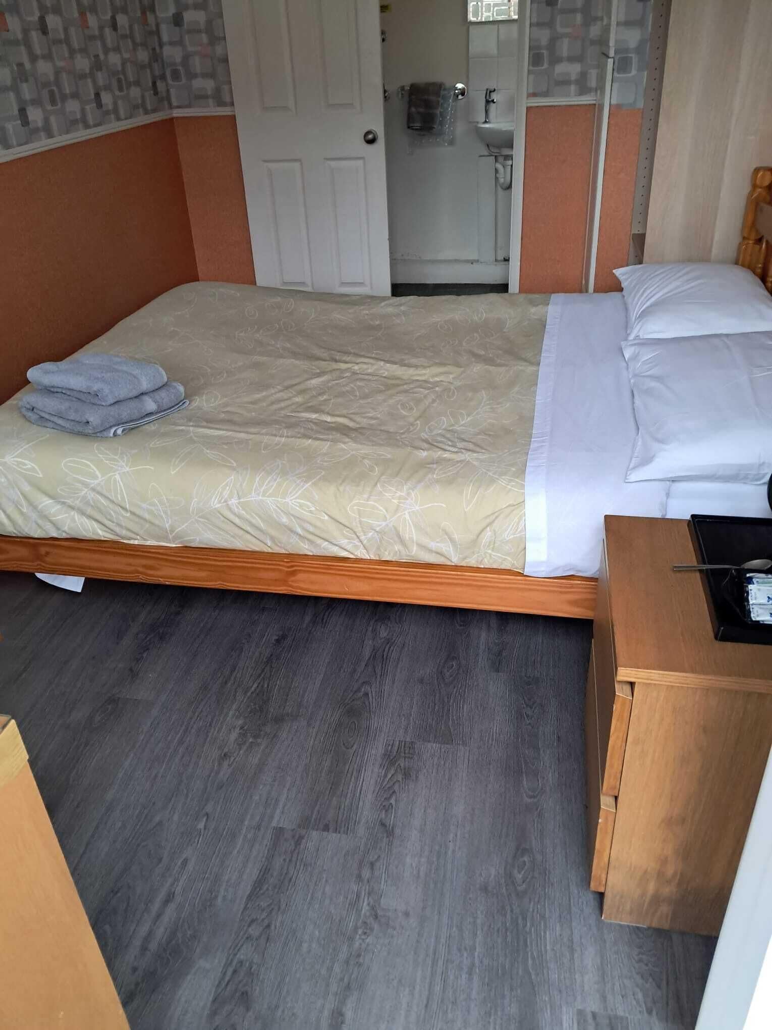 Une chambre d’hôtel avec un lit, une table de chevet en bois, une salle de bain visible à travers une porte ouverte et un mur orné d’un motif.