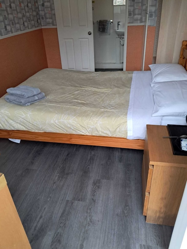 Ein Hotelzimmer mit Bett, einem Nachttisch aus Holz, einem durch eine offene Tür einsehbaren Badezimmer und einer Wand mit Muster.