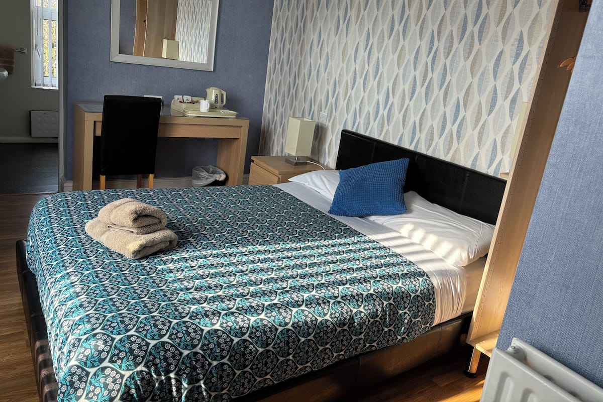 Una cama bien hecha con una colcha estampada, una almohada azul y una toalla doblada al lado.